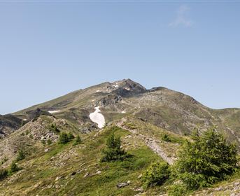 An impressive mountain landscape with gentle hills and snow-capped peaks. The sky is clear and blue, ideal for a hike in nature.