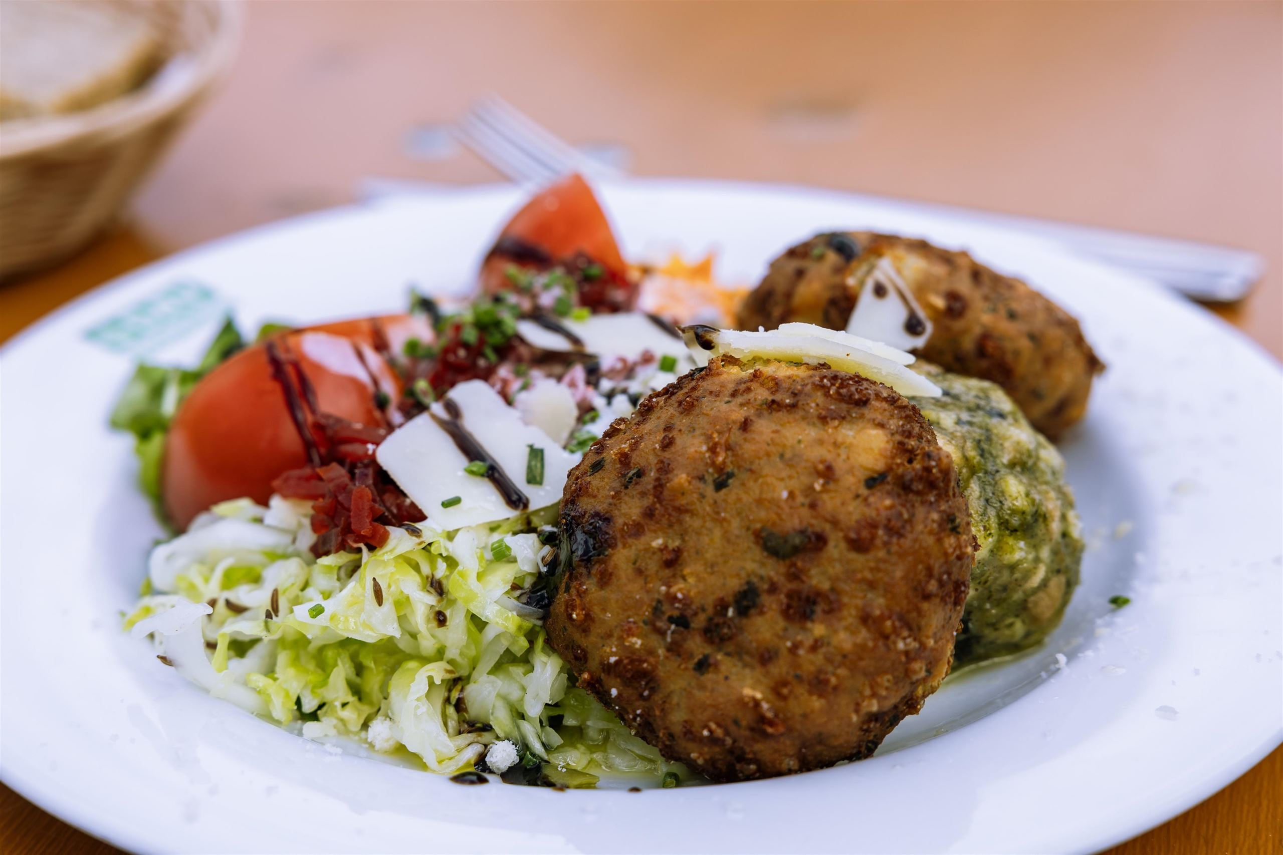 Ein Teller mit zwei knusprigen Gemüsefrikadellen und frischem Salat. Dazu geschnittene Tomaten und etwas Käse.