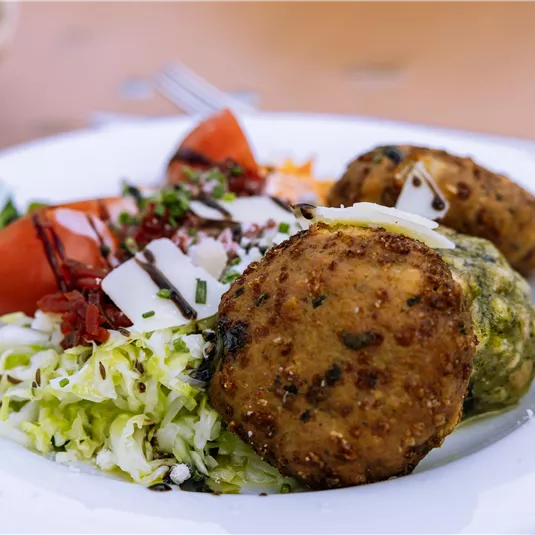 Ein Teller mit zwei knusprigen Gemüsefrikadellen und frischem Salat. Dazu geschnittene Tomaten und etwas Käse.