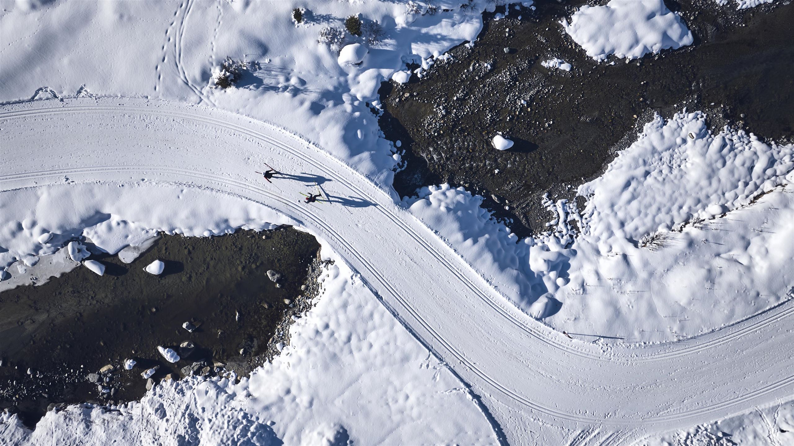 Eine kurvenreiche Schneestraße führt durch eine winterliche Landschaft. Im Hintergrund sind schneebedeckte Flächen und einige Felsen zu sehen.