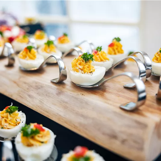 An appealing presentation of stuffed eggs on a wooden platter. The appetizers are nicely decorated and perfect for a buffet.