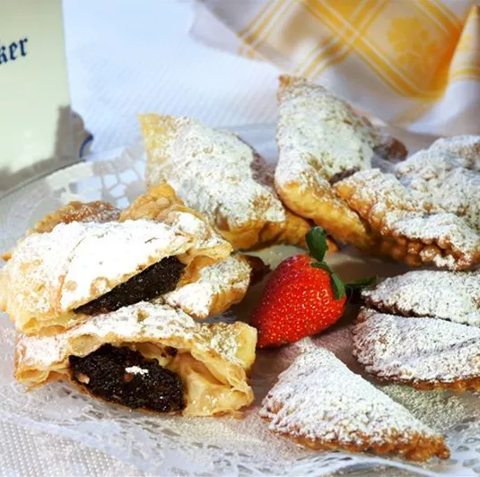 Eine Platte mit gebäckenen Leckereien, bestreut mit Puderzucker und einer Erdbeere. Im Hintergrund steht eine Zuckerdose.