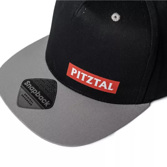 A black snapback cap with a gray visor.
On the front, the inscription "PITZTAL" is visible in red color.