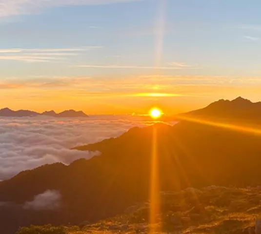 Ein wunderschöner Sonnenaufgang über den Bergen, verborgen hinter einer Wolkenschicht. Die goldenen Strahlen der Sonne erleuchten die Landschaft.
