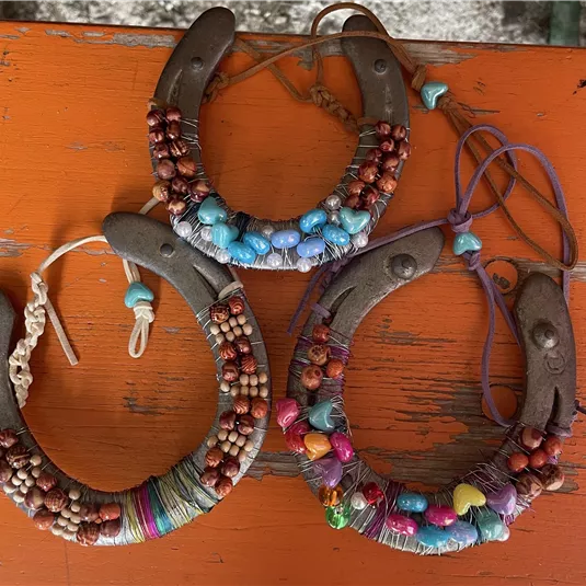Three creative pieces of jewelry made from wood and colorful beads are lying on an orange surface. Each piece has a unique design and combines different materials and colors.