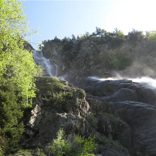 A beautiful waterfall cascades over rocky cliffs. Surrounded by green trees and radiant sunlight.