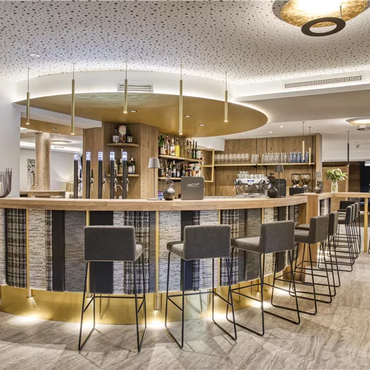 An elegant bar with modern chairs and a stylish bar counter. The atmosphere is inviting and well-lit.