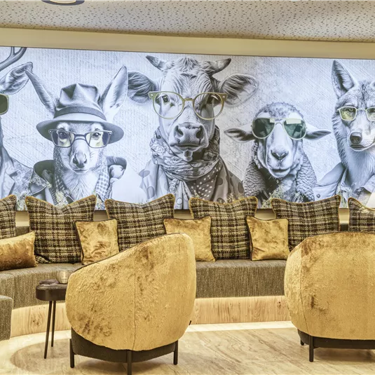 A modern room with comfortable sofas and a large wall featuring an artwork of animals in sunglasses. The animals are presented in a stylish and appealing way, creating a creative atmosphere.