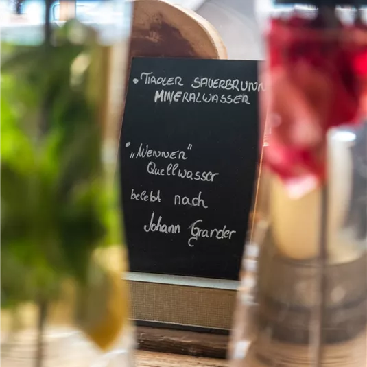 A selection of flavored water in glass carafes is ready. In the background, there is a board with the description of the offerings.