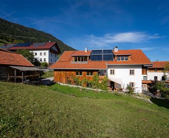 A picturesque alpine landscape with traditional houses and green grass. In the background, there are mountains and a clear blue sky.