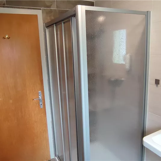 Ein modernes Badezimmer mit einer Duschkabine und einem Waschbecken. Die Wände sind hell gefliest und es gibt einen Holz-Haustür.