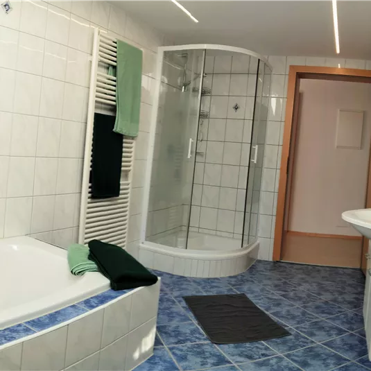 A modern bathroom with a bathtub and a shower. The walls are tiled, and there are green towels as well as a light-colored flooring.