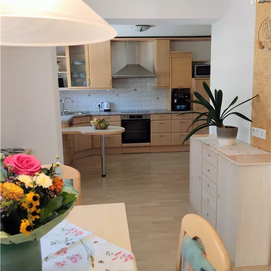 A cozy kitchen area with wooden cupboards and bright walls. A bouquet of flowers on the table makes the room friendlier.