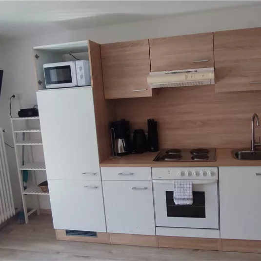 Eine moderne Küche mit Holzregalen und weißen Schränken. Sie ist gut ausgestattet mit Herd, Mikrowelle und Kühlschrank.