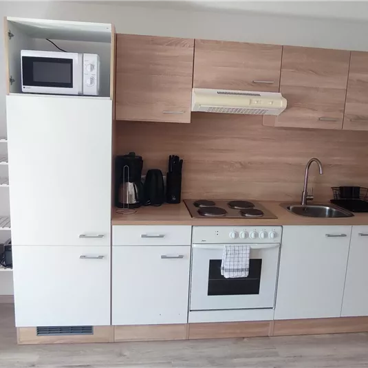 Eine moderne Küche mit Holzregalen und weißen Schränken. Sie ist mit einem Herd, einer Mikrowelle und anderen Küchengeräten ausgestattet.