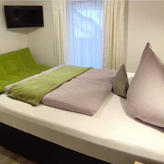 Ein gemütliches Schlafzimmer mit einem Doppelbett und einem Schlafsofa. Der Raum hat große Fenster und eine moderne Dekoration.