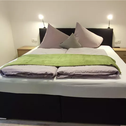 Ein gemütliches Schlafzimmer mit einem großen Bett und dekorativen Kissen. Der Raum ist hell und modern eingerichtet.