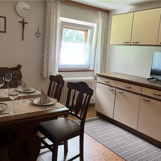 A cozy kitchen with a dining table set for dinner. In the background, there are white kitchen cabinets and a television visible.