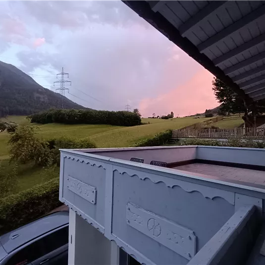 A peaceful landscape with gentle hills and a colorful sky. In the foreground, there is a balcony with a wooden cladding.
