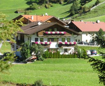 A picturesque house surrounded by green meadows and mountains. Flowers adorn the windows and a peaceful atmosphere shapes the scene.