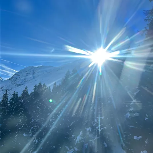 A sunny winter landscape with snow-covered mountains and a unique refraction of light. The clear blue sky enhances the beauty of the surroundings.