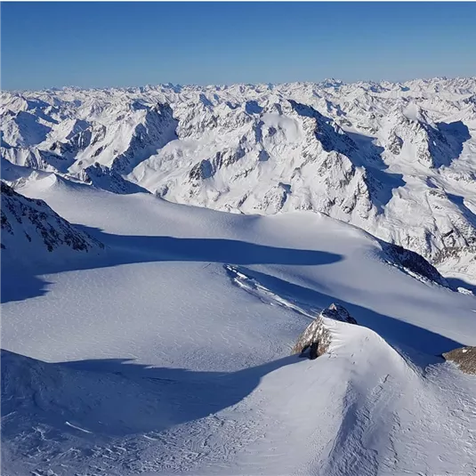 An impressive mountain landscape with snow-covered peaks and a large glacier. The clear sky makes the majestic scenery shine.