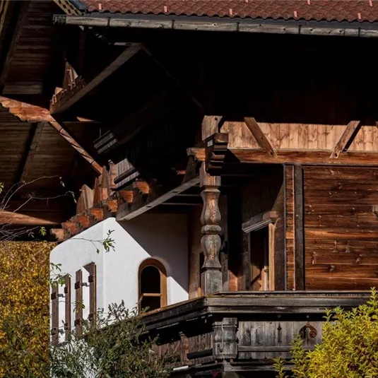 A traditional wooden house with a characteristic balcony. Surrounded by trees and autumn leaves.