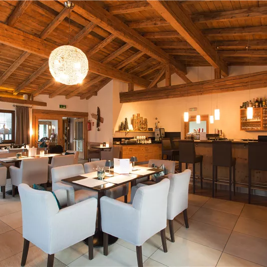 A modern restaurant with a wooden ceiling and elegant seating areas. The bar is well-equipped and the atmosphere feels inviting.