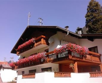 A charming house with blooming balcony boxes. The facade is bright and inviting, surrounded by clear blue sky.