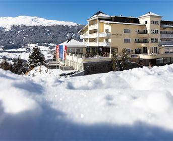 Ein gemütliches Hotel in einer winterlichen Landschaft. Schnee bedeckt den Boden, während die Berge im Hintergrund strahlen.