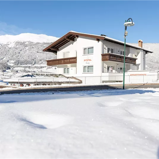A white building in a snowy landscape. In the background are snow-covered mountains and a blue sky.