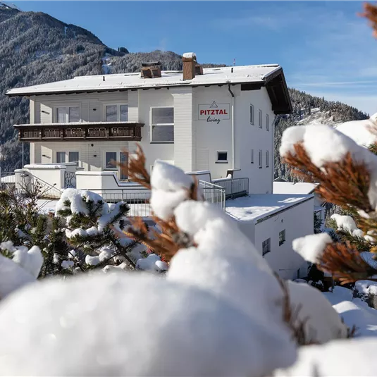 A snow-white building surrounded by snow-covered trees. In the background, snow-covered mountains are visible.