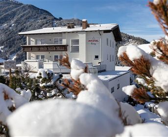 Ein schneeweißes Gebäude umgeben von schneebedeckten Bäumen. Im Hintergrund sind schneebedeckte Berge sichtbar.