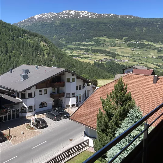 Eine malerische Aussicht auf die Berge mit schneebedeckten Gipfeln und idyllischen Häusern. Der Himmel ist klar und blau, was die friedliche Landschaft unterstreicht.