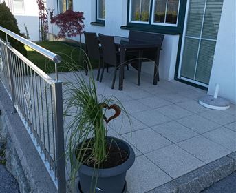 Eine gemütliche Terrasse mit einem Tisch und Stühlen. Eine Pflanze in einem Topf mit Herzform verleiht dem Platz Charm.
