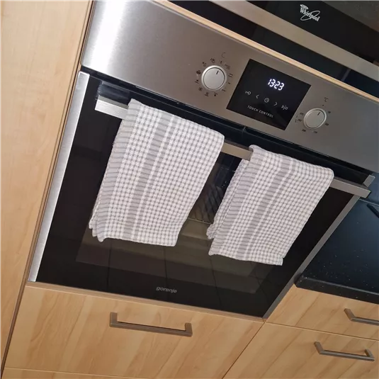 A modern kitchenette with a built-in oven and two dish towels. The oven has a digital display and an elegant stainless steel surface.