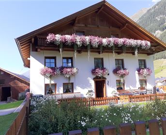 A traditional house in the mountains with beautiful flowers at the windows. Surrounded by a green meadow and a picnic bench in the garden.