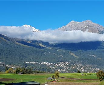 Eine beeindruckende Berglandschaft mit schneebedeckten Gipfeln und grünem Tal. Der Himmel ist klar und blau, was die natürliche Schönheit der Umgebung betont.