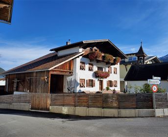 A charming, traditional house with flower boxes. The surroundings are rural and tranquil, with a clear sky.