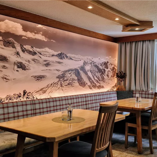 Eine gemütliche Stube mit Holztischen und Bänken. An der Wand befindet sich eine große Landschaftsaufnahme der Berge.