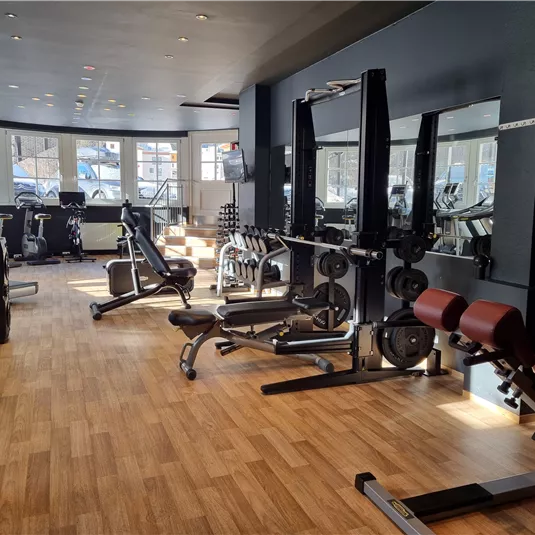 A modern gym with various workout equipment. Large windows provide plenty of daylight and a welcoming atmosphere.