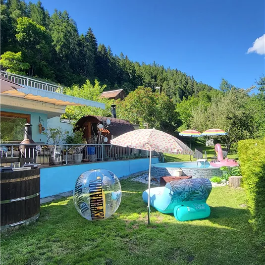 Ein schöner Garten mit einem Pool und Liegen. Im Hintergrund sind Bäume und eine Terrasse zu sehen.