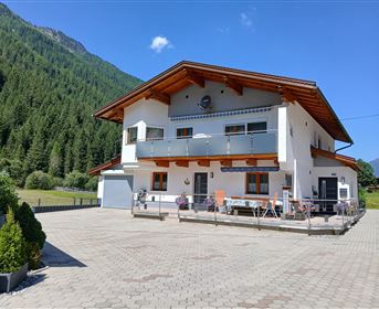 Ein modernes Haus in den Bergen mit einem großen Außenbereich. Die Umgebung ist von grünen Wäldern und Hügeln umgeben.