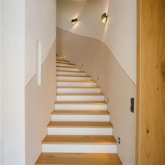 A beautiful staircase with white steps and wooden cladding leads upwards. The walls are bright and modernly designed.