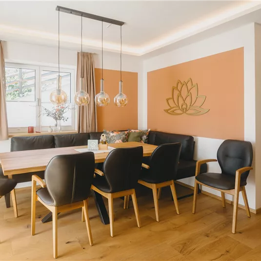 A modern dining room with a large wooden table and black chairs. The walls are painted in warm colors, and a stylized lotus flower is decoratively placed.