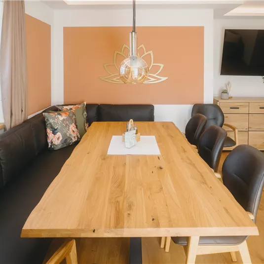 A modern-designed dining area with a large wooden table and comfortable chairs. The walls are in warm colors, and a decorative wall design complements the space.