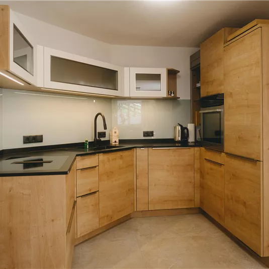 A modern kitchen with wooden surfaces and a black workspace. It features a built-in stove and ample storage space.