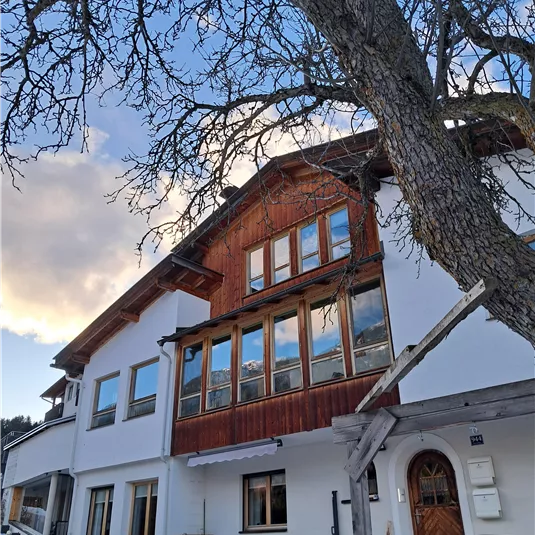 Ein modernes Haus mit Holzverkleidung und großen Fenstern. Es steht unter einem blauen Himmel mit einigen Wolken.