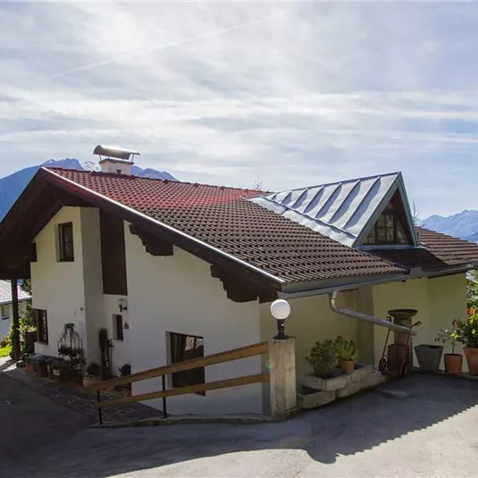 A beautiful house with a modern roof, surrounded by mountains and trees. The clear landscape offers a calm and peaceful atmosphere.