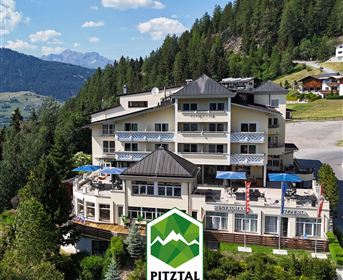 Ein panaromatisches Hotel umgeben von Bäumen und Bergen. Die Terrasse hat blaue Sonnenschirme und bietet einen schönen Blick auf die Landschaft.